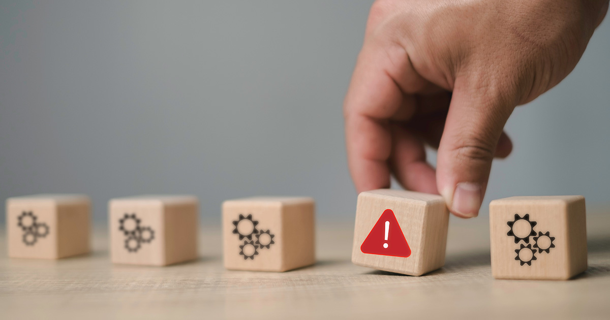 A hand picking out a wooden block with a warning symbol from a set of blocks, symbolizing the identification of problems, risk management, and problem detection in the process.