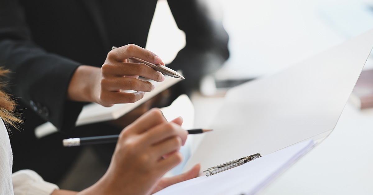 Close-up: Two women consult with each other using files and documents.